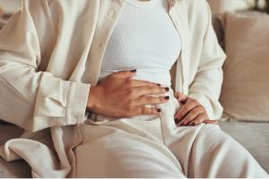 Woman, hands and stomach pain on sofa with gas, bloating or IBS in home. Person, abdomen with constipation, nausea and digestion problem on couch in lounge