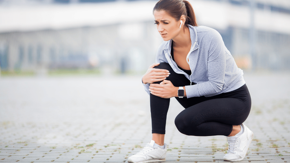 Woman experiencing leg cramp pain while exercising outdoors, holding her knee