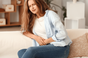 Woman on a couch, grasping her stomach with lower abdominal pain